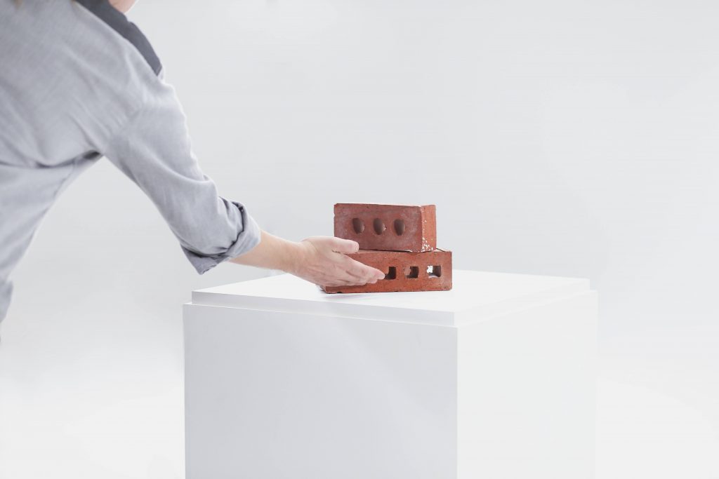Person presenting a stack of two bricks in a white room